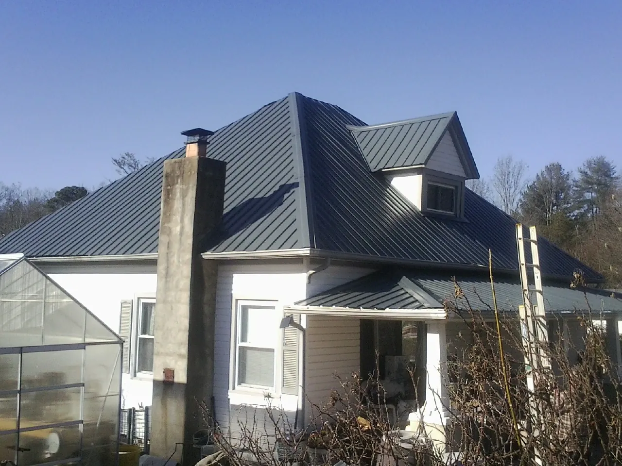Dark blue standing seam metal roof on a white farmhouse with dormer — Slate & Tile Roof Repair by Roofing Brothers in Butner