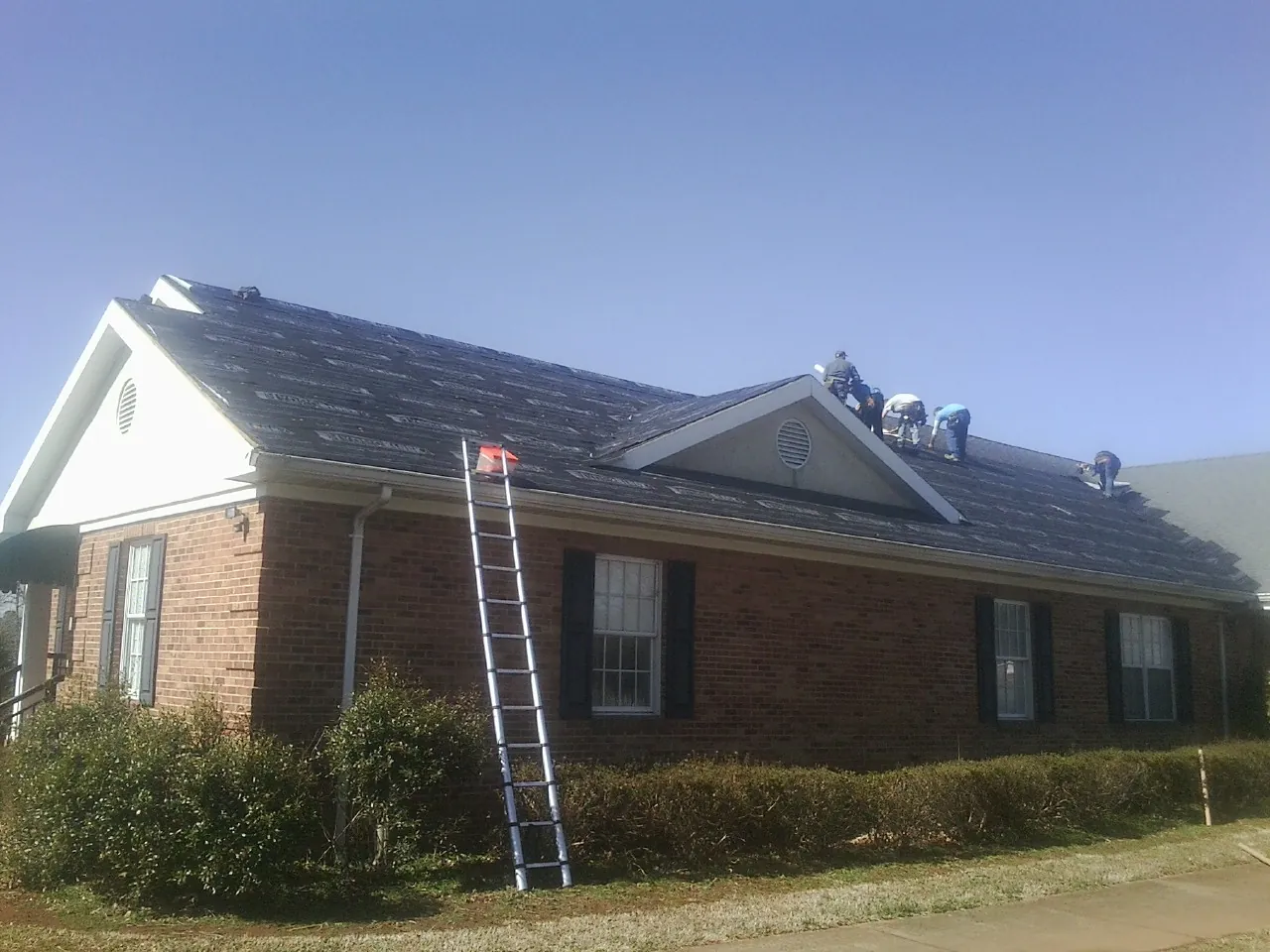 Crew tearing shingles off a brick ranch roof with a ladder set — Emergency Roof Repair work by our crew in Butner