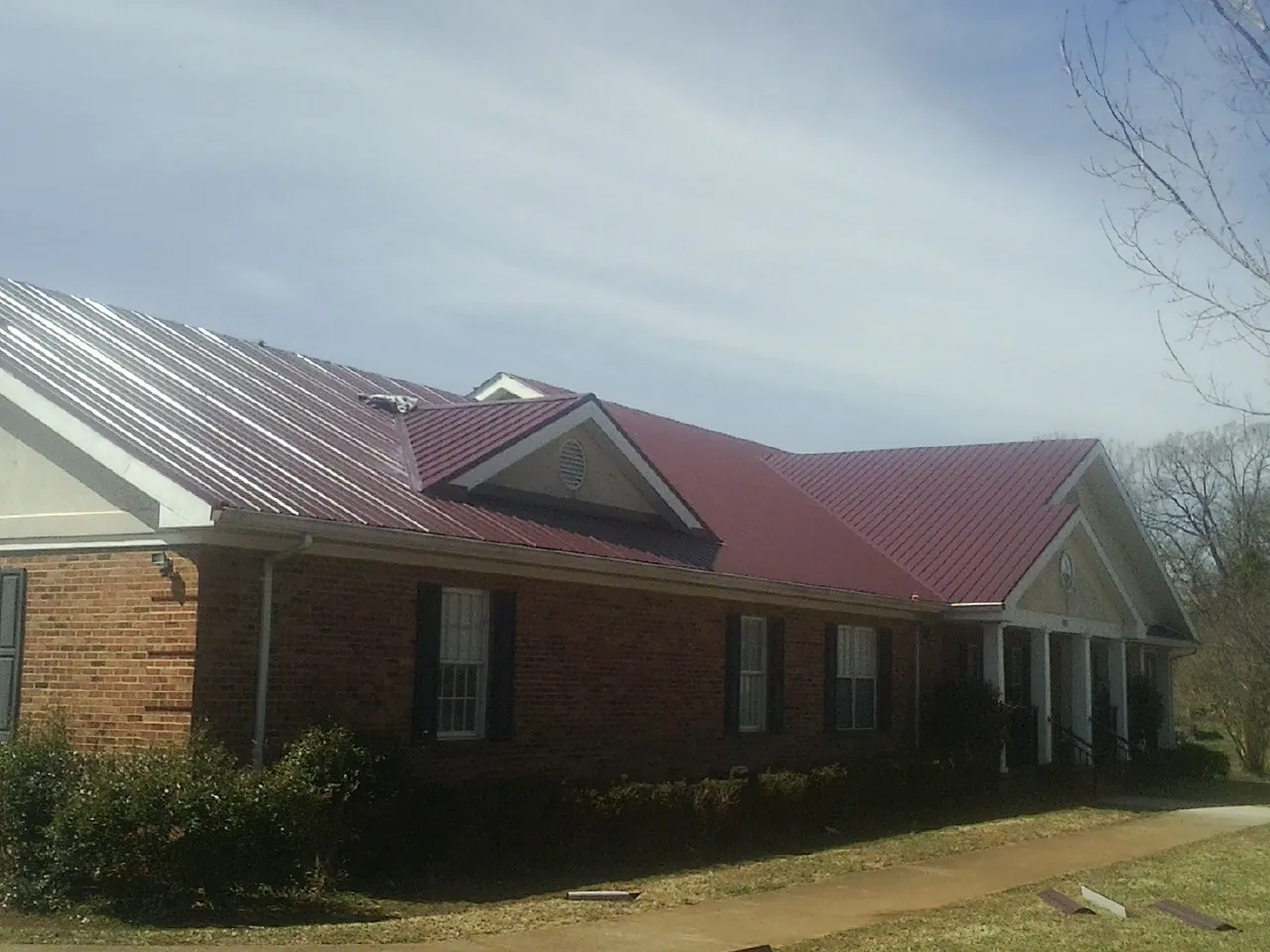 Red metal roof with gabled entries on a long brick building, from a Hail Damage Roof Repair job in Butner