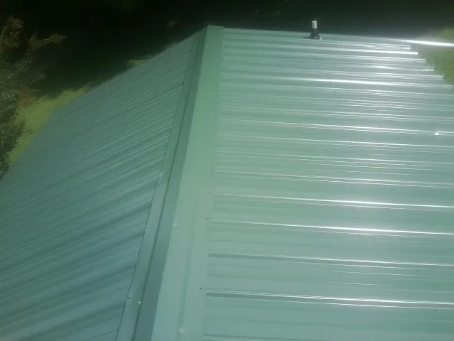 New green metal panels meeting at the ridge of a roof — Flat Roof Repair work by our crew in Butner