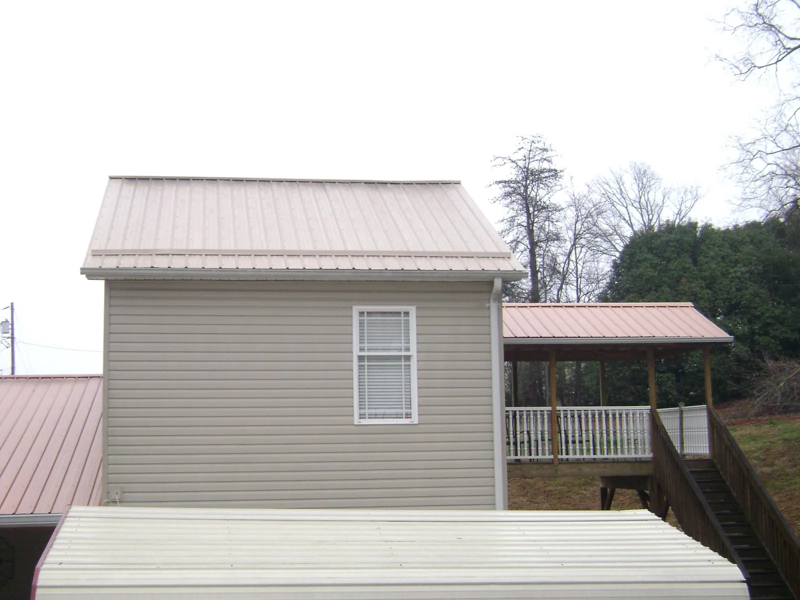 Tan metal roofs on a two story addition and attached porch, from a Roof Replacement job in Butner
